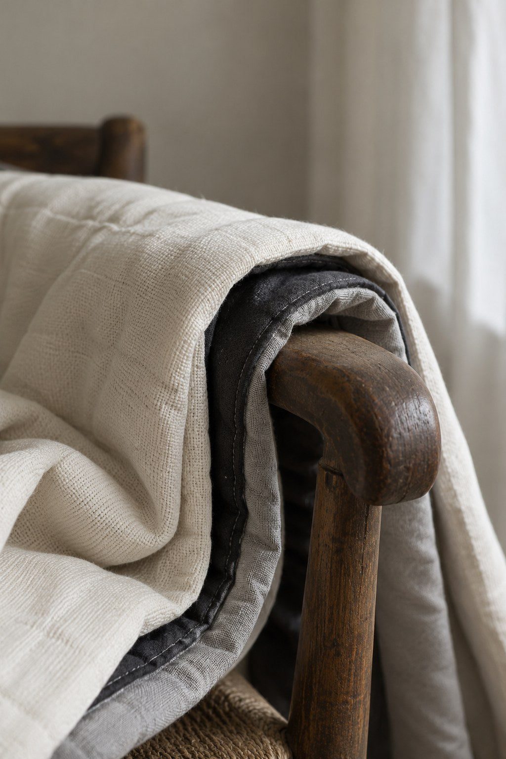Coin d'un rideau blanc cassé triple couche posé sur le bras d'une chaise en bois