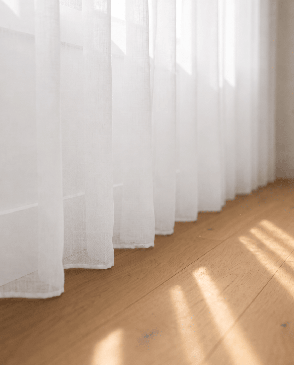 Bas du voilage transparent blanc sur parquet, rayons de soleil