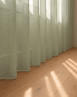 Bas du voilage vert pistache sur parquet, rayons de soleil