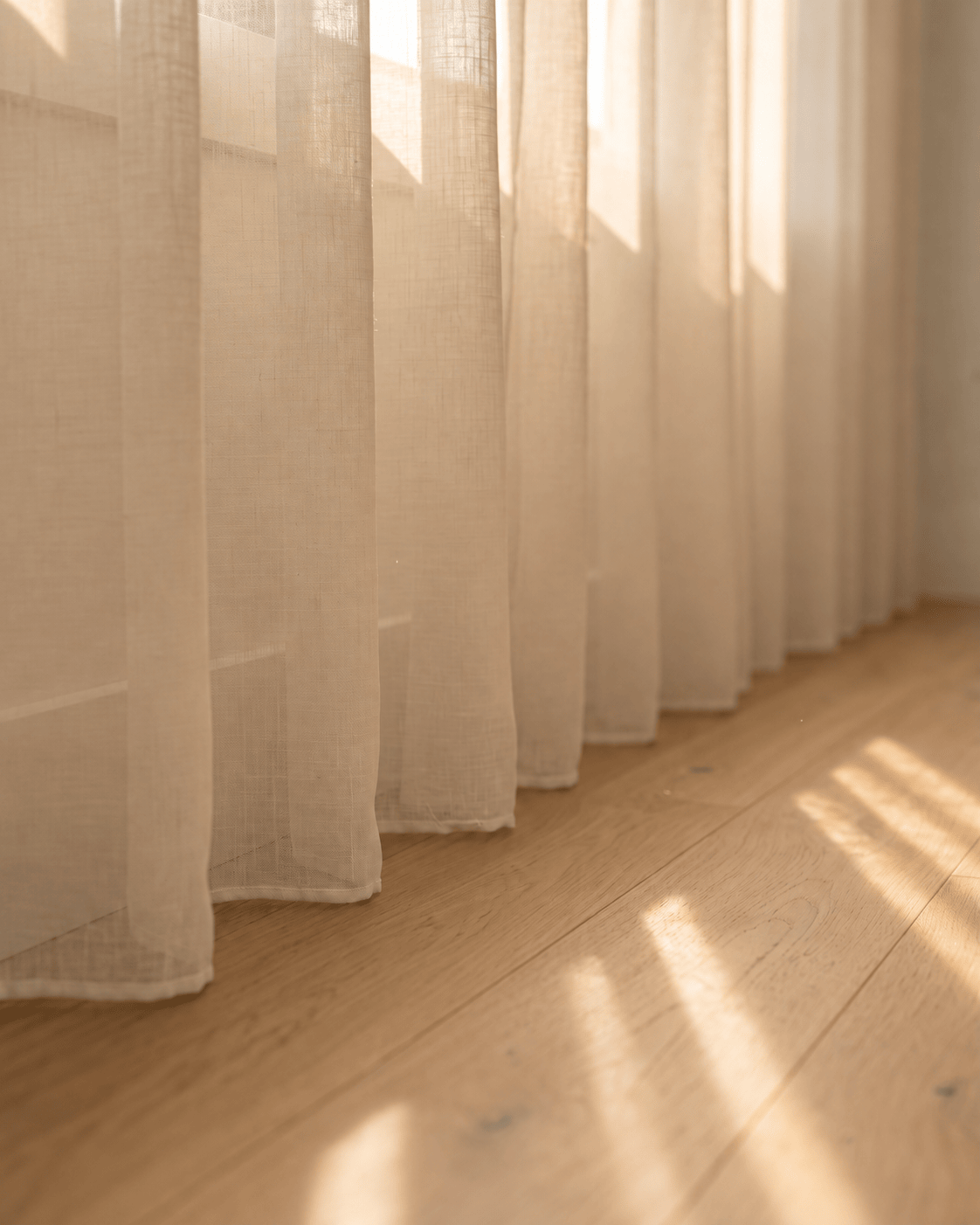 Bas du voilage beige sur parquet, rayons de soleil