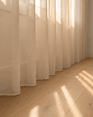 Bas du voilage beige sur parquet, rayons de soleil