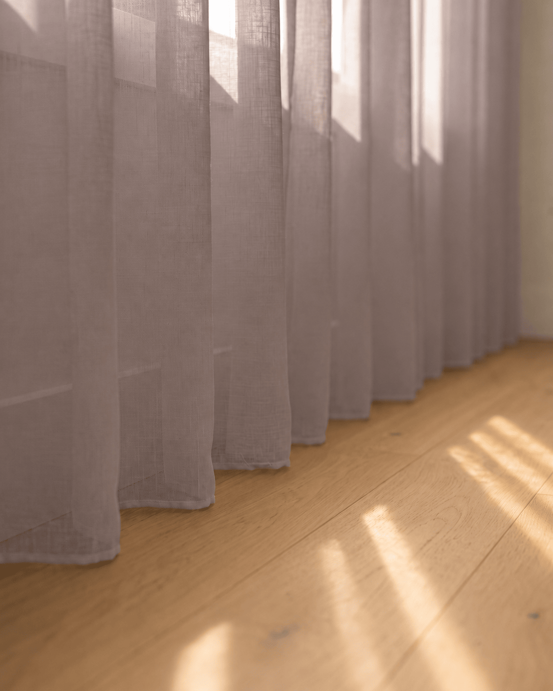 Bas du voilage gris mauve sur parquet, rayons de soleil