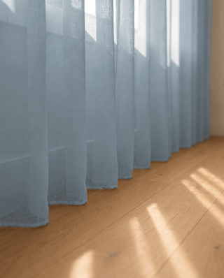 Bas du voilage bleu ciel sur parquet, rayons de soleil